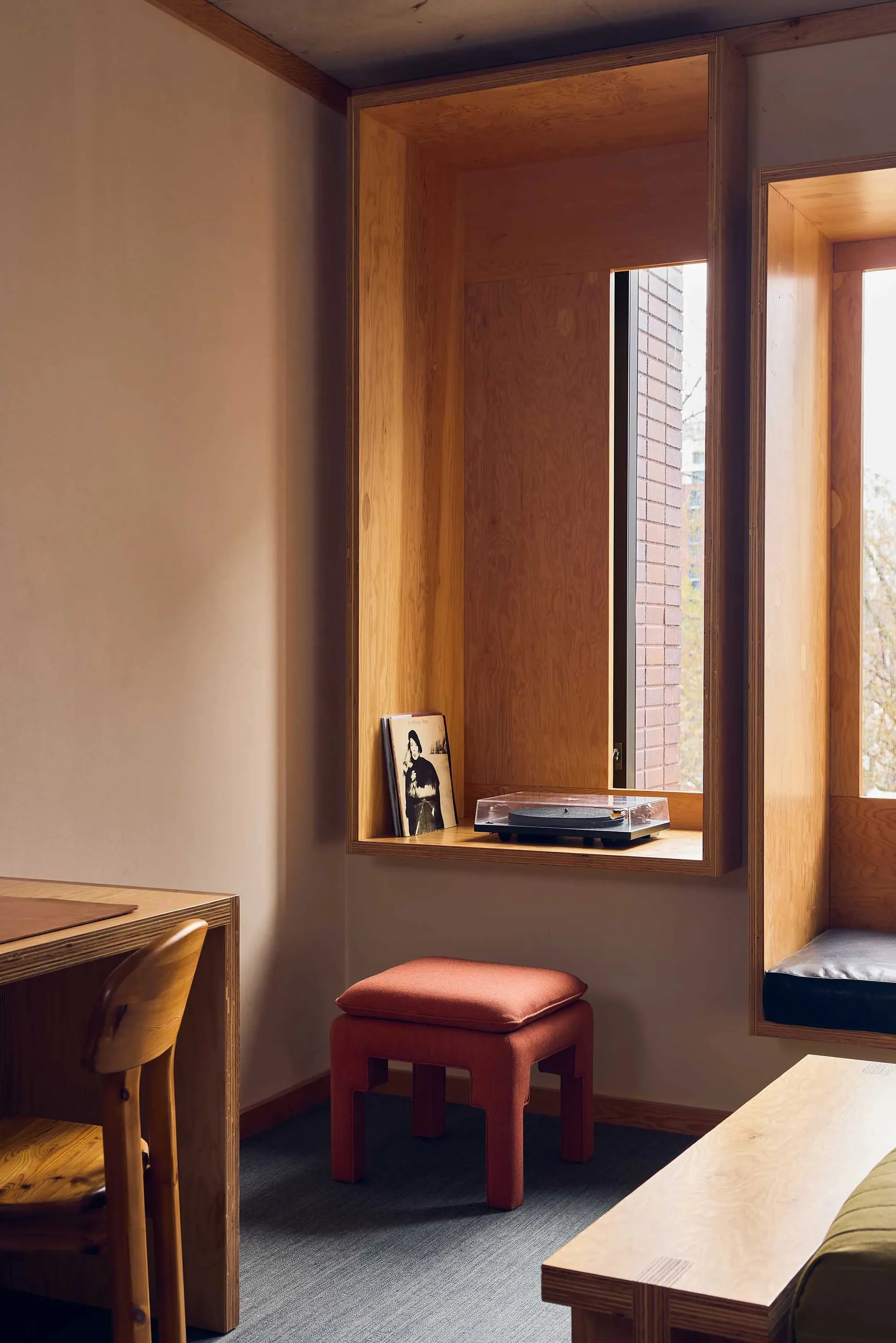 A minimalist residential interior featuring wooden furniture and a wooden window frame near a wooden table.