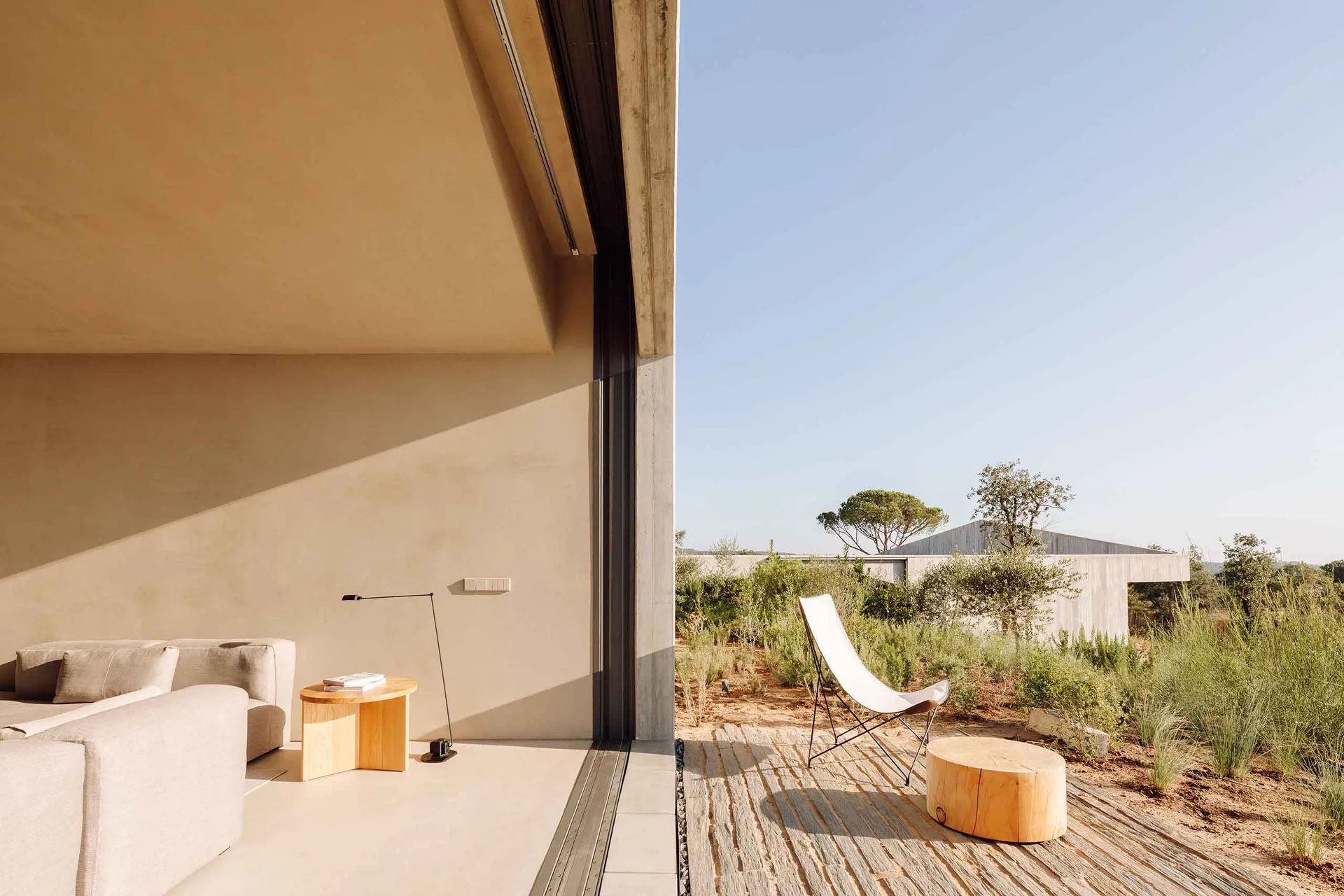 Modern minimalist patio area with concrete flooring and furniture, adjacent to natural landscape.
