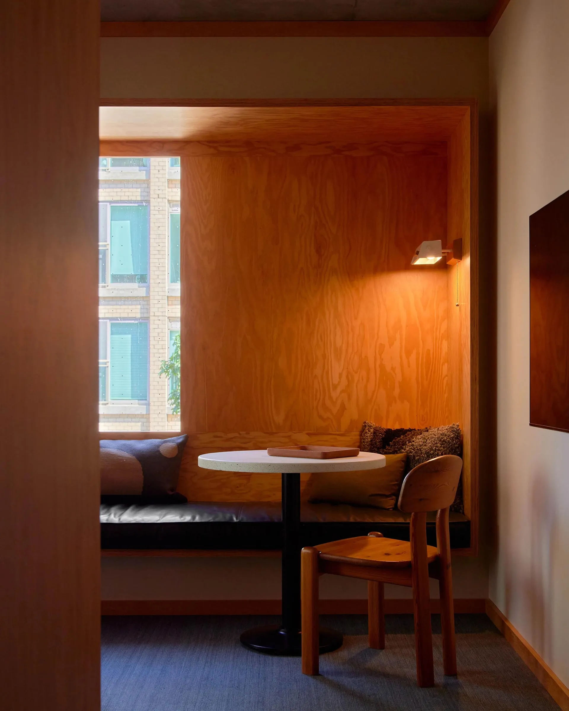 A modern minimalist living room with wooden elements and a cozy seating area by a window.