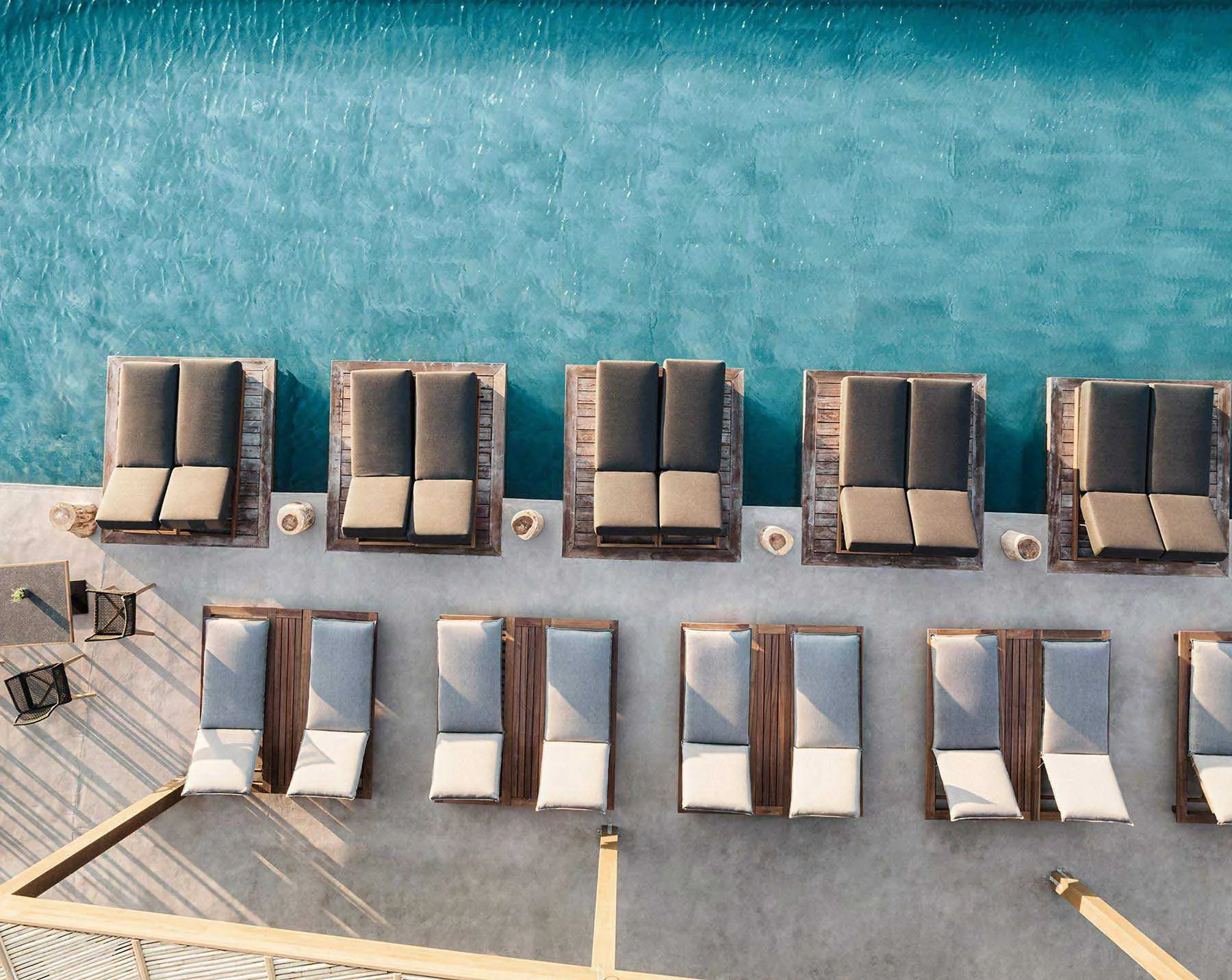 Aerial view of a poolside seating area with wooden loungers and cushions.
