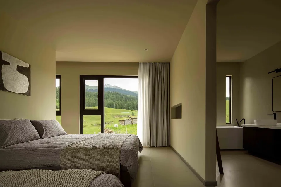 A modern minimalist bedroom featuring neutral-toned decor, a cozy bed, and a floor-to-ceiling window overlooking a green land