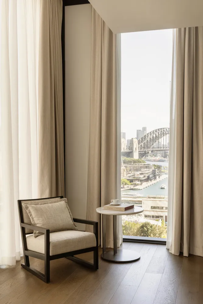 A minimalist living room with neutral-toned furnishings and large windows overlooking a cityscape.