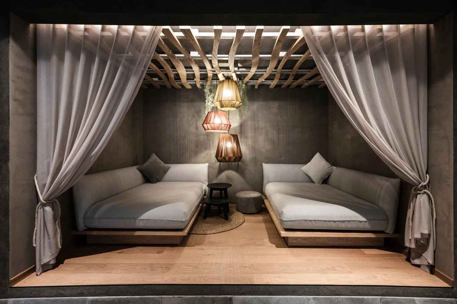 A minimalist living space with gray sofas, wooden flooring, and a warping wood ceiling.