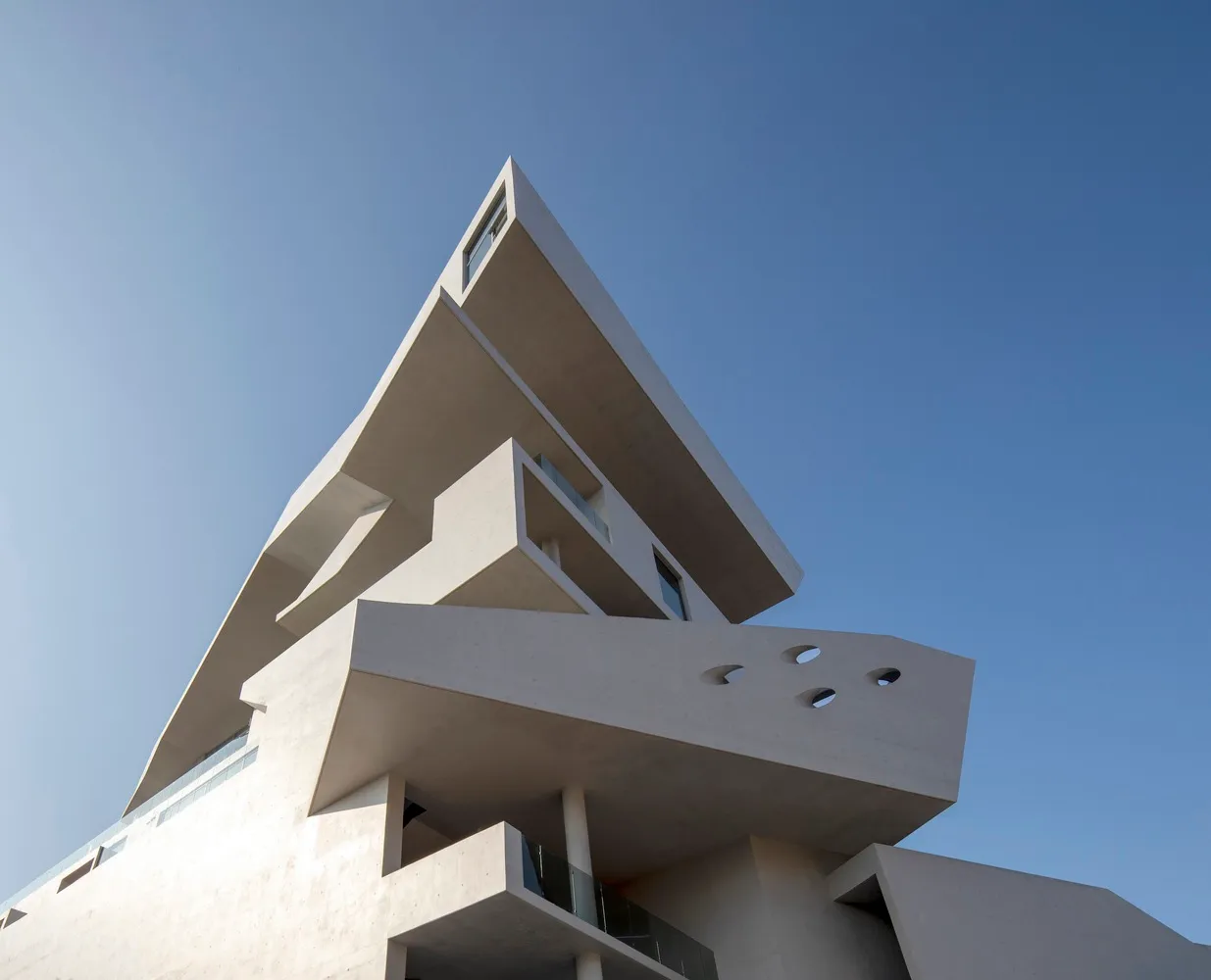 A modern architectural design featuring white concrete structures against a clear blue sky.