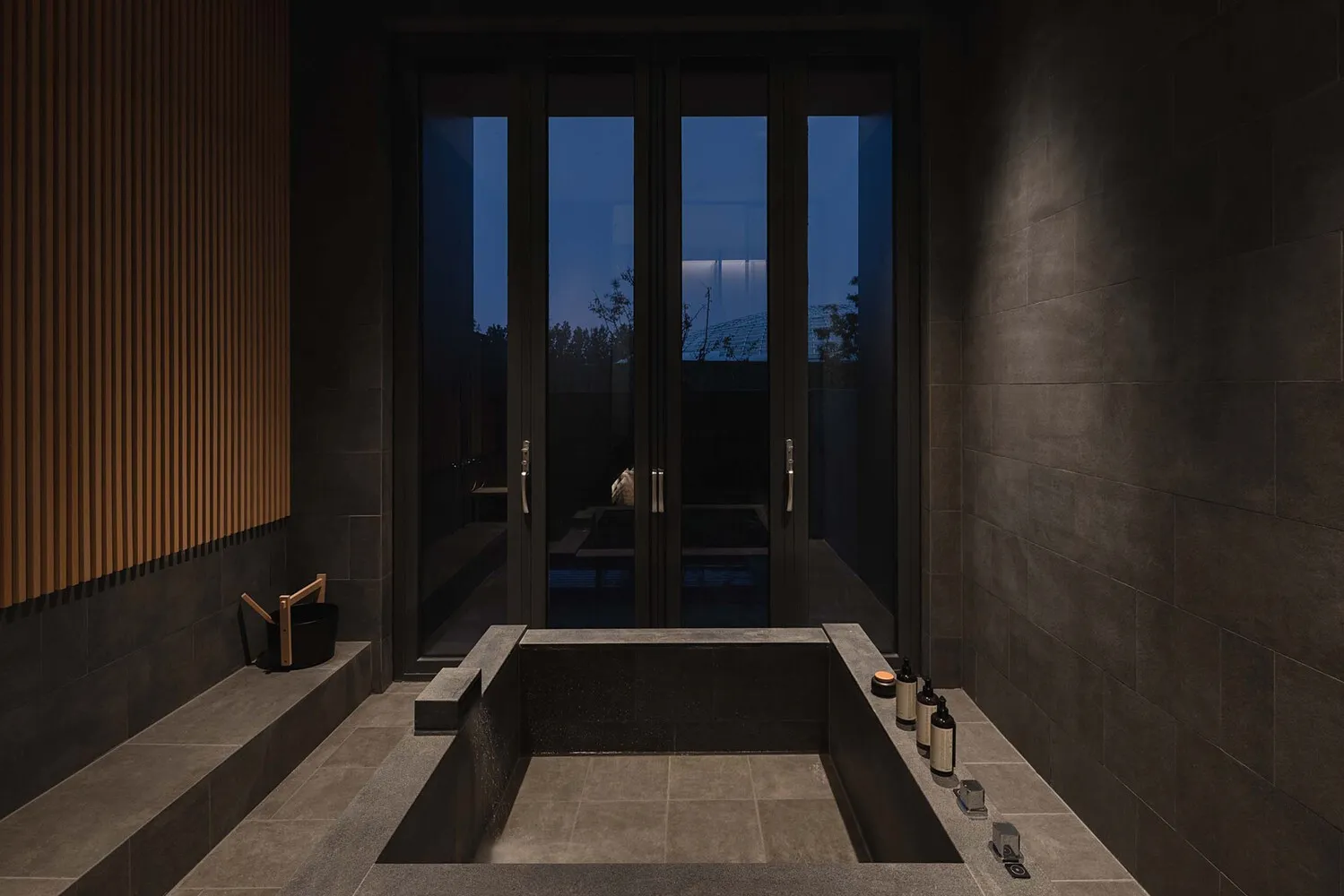 Concrete modern bathroom with glass doors and a view of the outdoors at dusk.