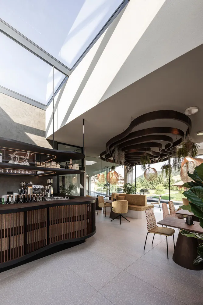 A modern cafe bar with a glass ceiling, wooden counter, and metal chairs.