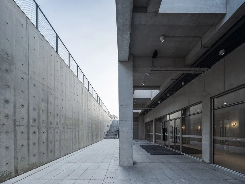 Modern commercial space featuring a minimalist design with concrete walls, a spacious walkway, and large glass doors.