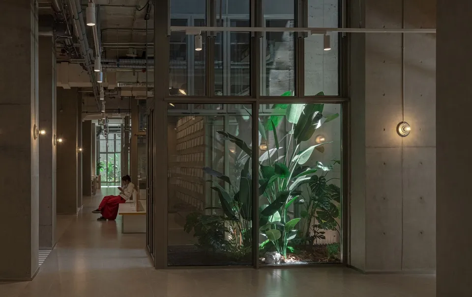 A modern industrial corridor features concrete walls, glass partitions, and green plants.