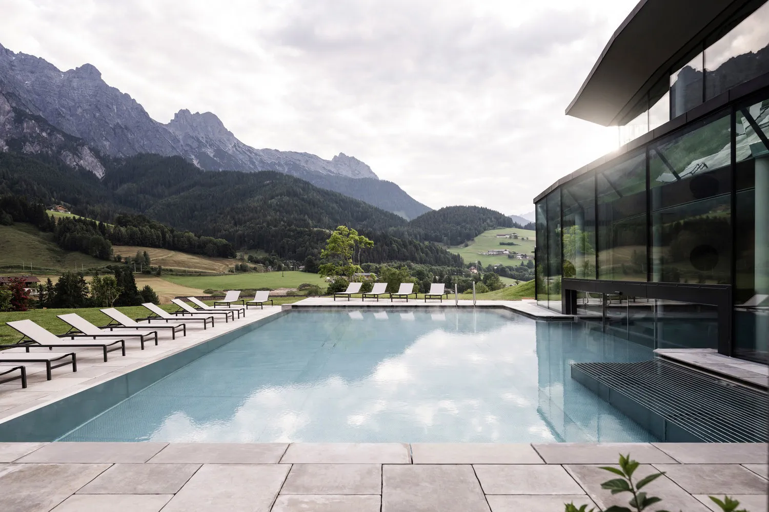 Modern outdoor swimming pool with lounge chairs and a mountainous landscape in the background.