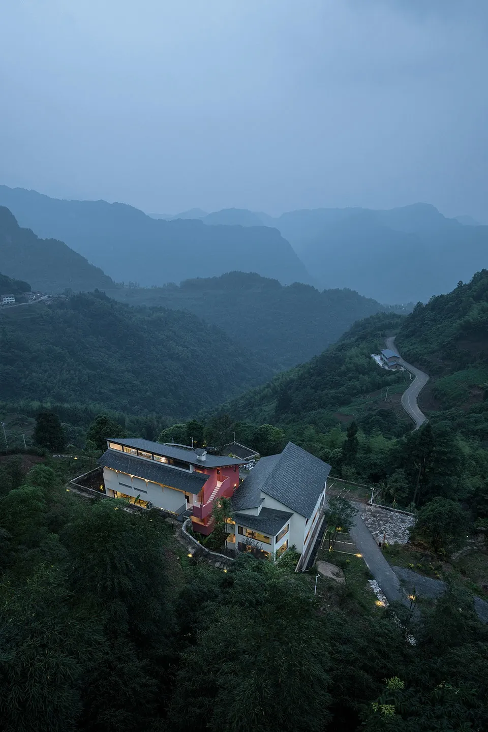 現代住宅建築以混凝土與玻璃為主材，背景為茂密綠丘與山巒