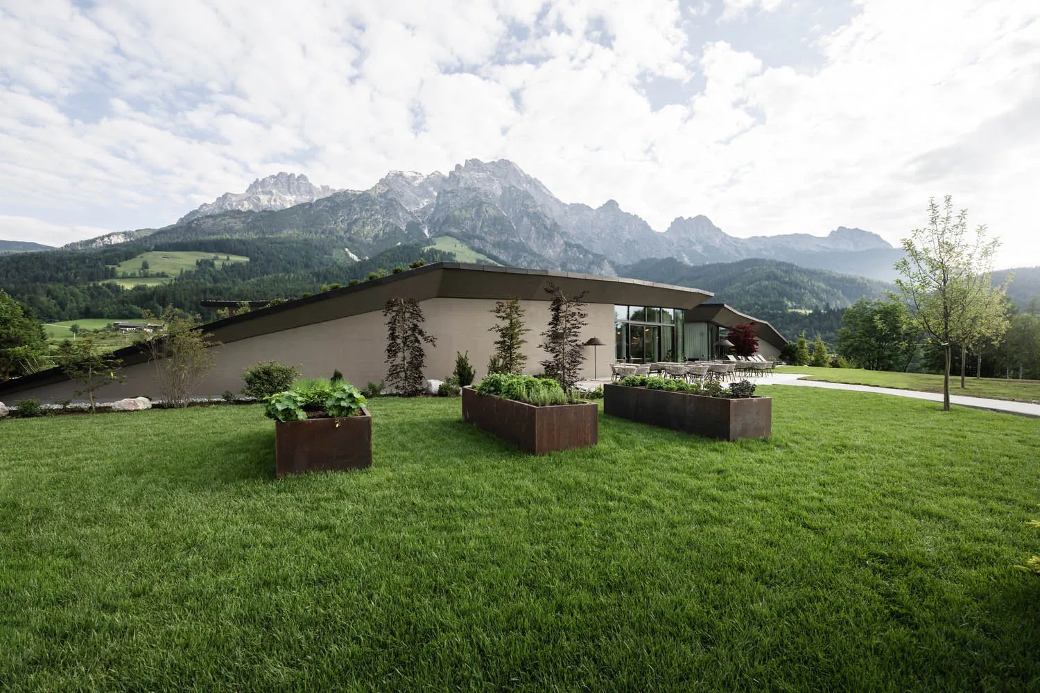 A modern residential exterior with greenery in planters and mountains in the background.