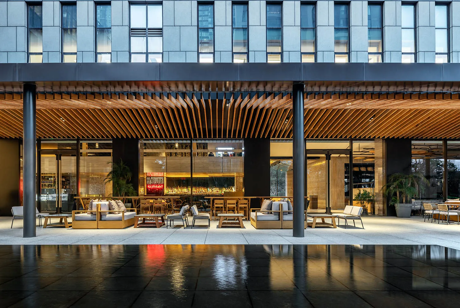 A modern restaurant interior featuring wooden tables and chairs, glass walls, and metal accents.