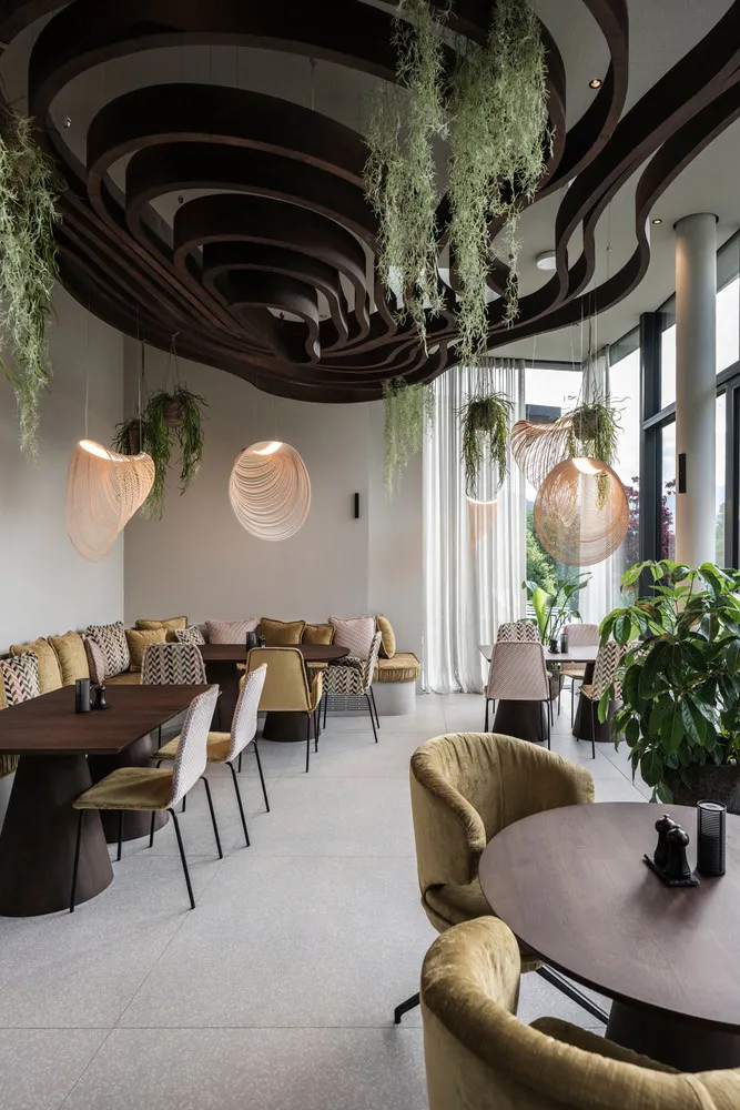 Contemporary restaurant interior featuring a wooden ceiling with circular design elements, hanging plants, and a mix of seati