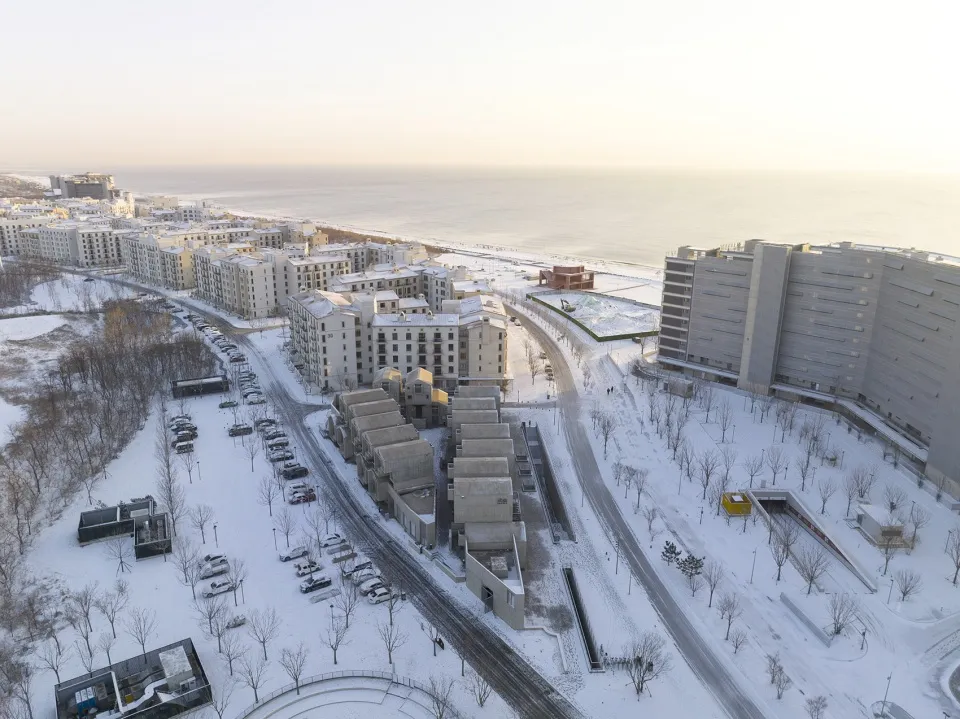 Aerial view of a snow-covered residential area with apartment buildings and a beach in the background.