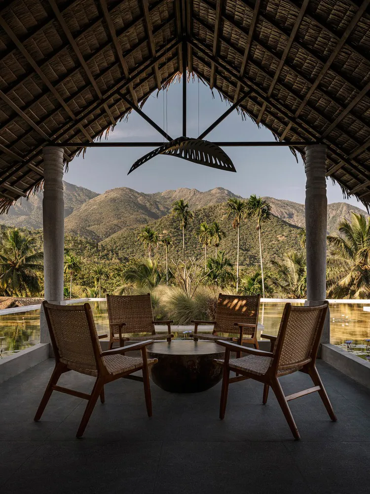 Outdoor seating area with woven bamboo furniture overlooking mountains and palm trees.