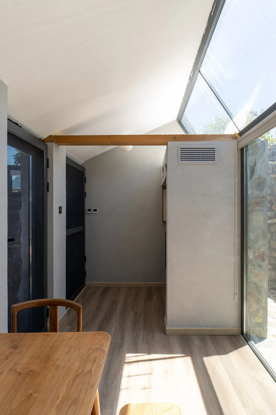 A minimalistic interior space featuring a wooden floor and a window with sunlight streaming in.