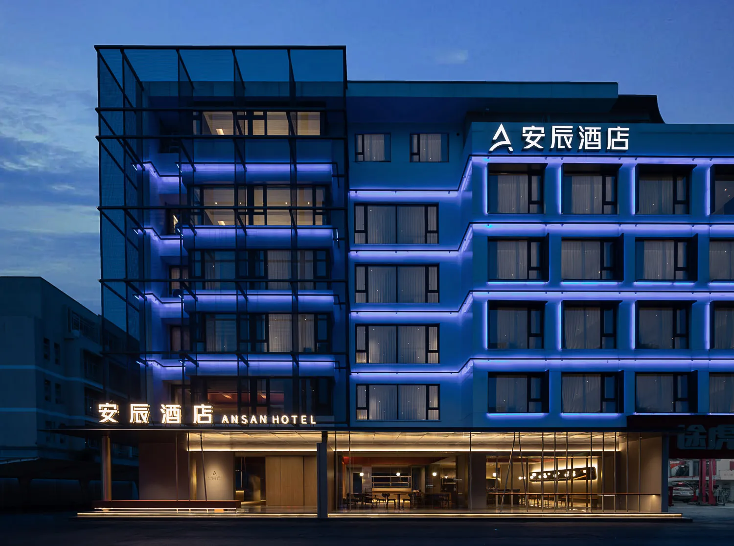 Modern hotel exterior with metallic frame, glass paneling, and blue lighting during twilight.