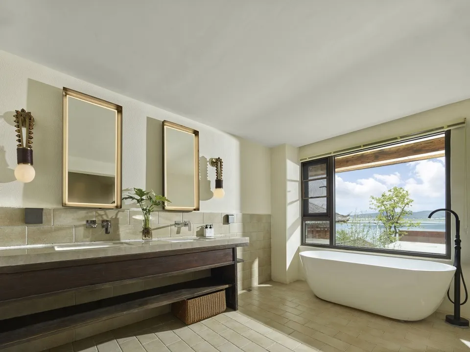 Modern minimalist bathroom featuring ceramic tiles, a large window with a view, a freestanding bathtub, and a double sink van