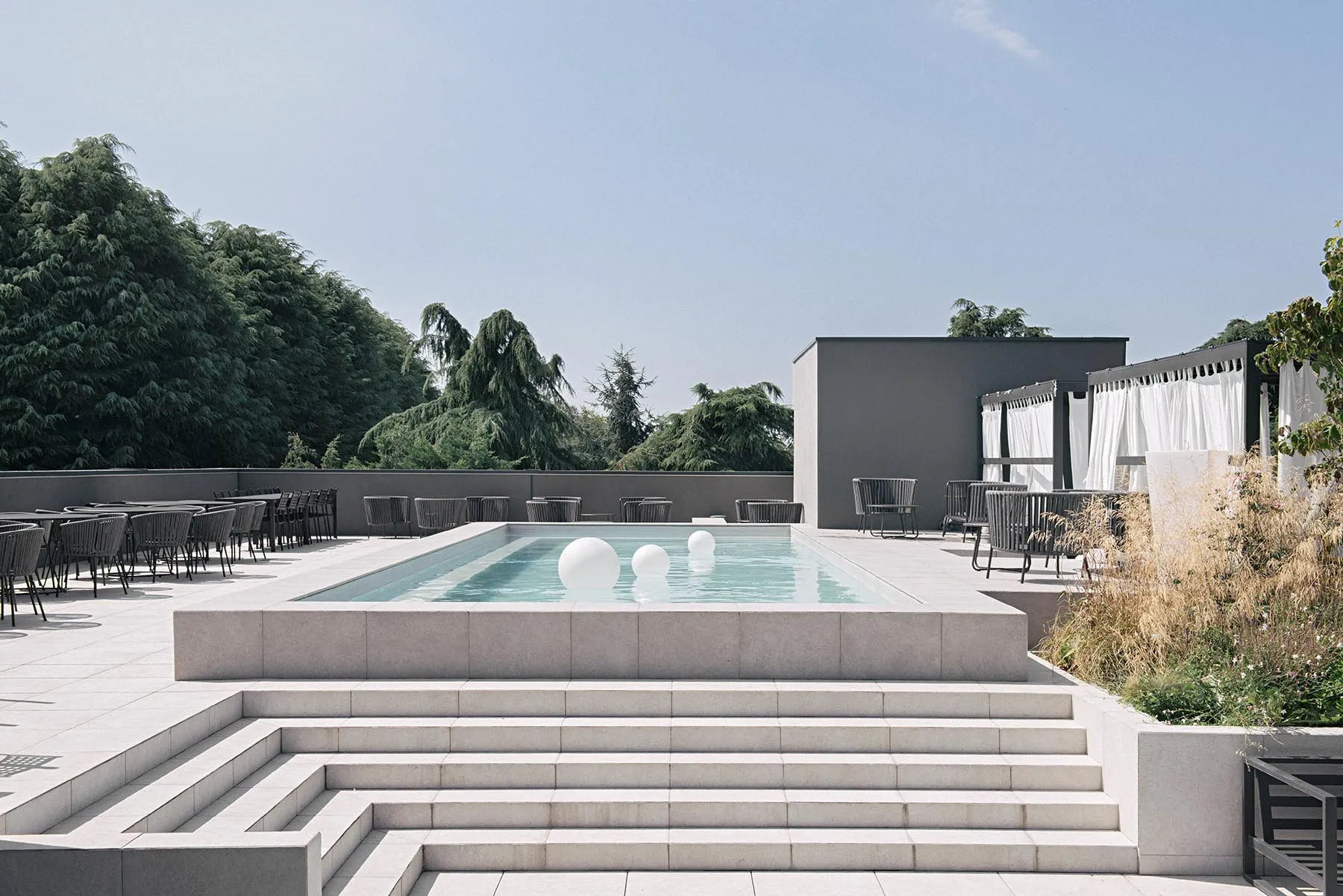 Modern outdoor swimming pool with concrete surroundings and white spherical buoy floating in the water.