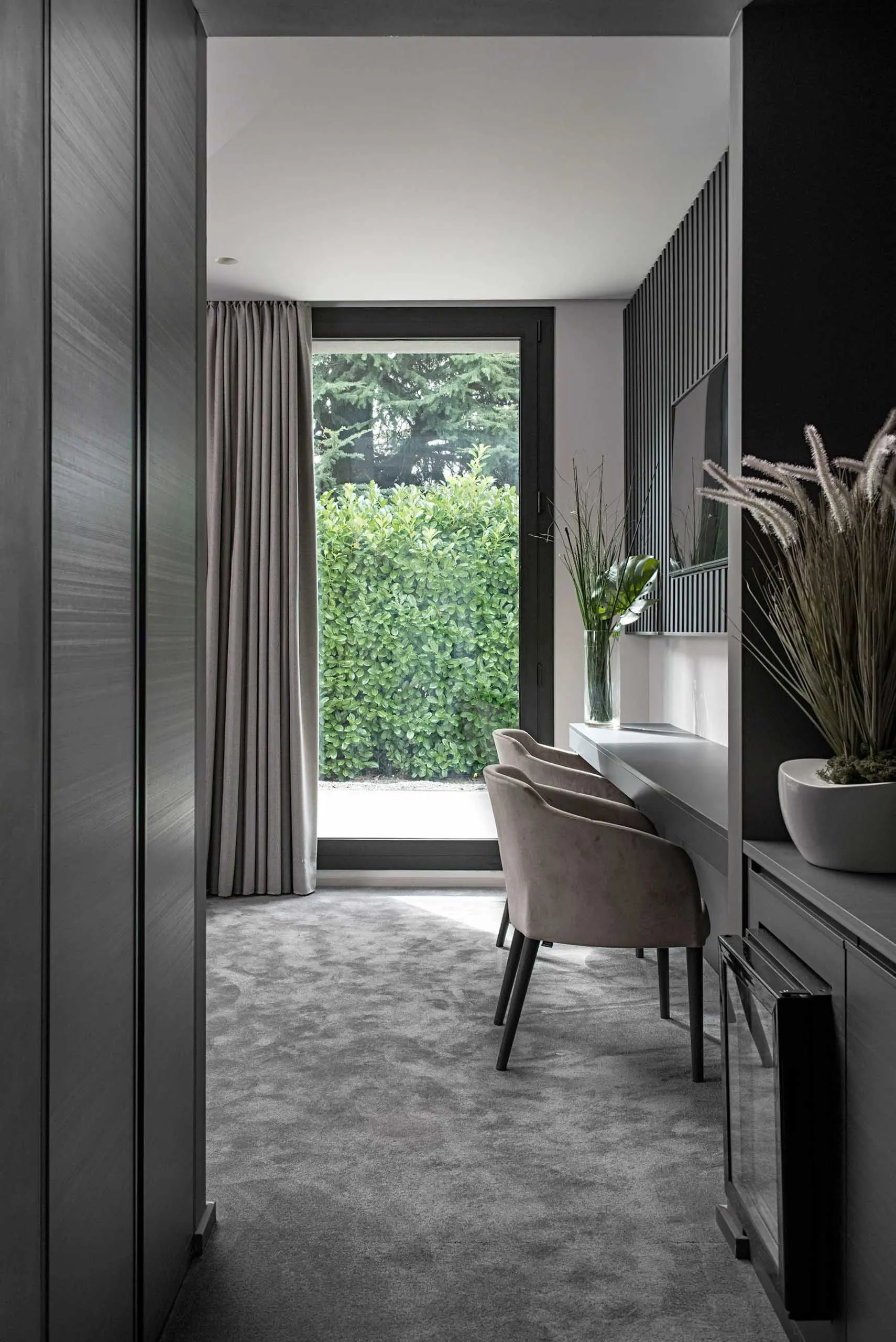 A modern dining room featuring grey tiles and concrete elements, with a large window providing natural light.