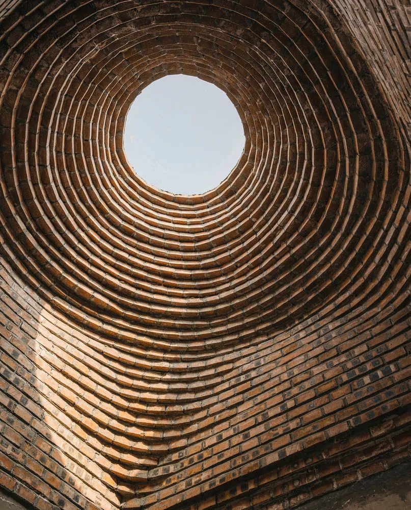 A deep, circular brick tunnel viewed from below, leading upwards to an open sky.
