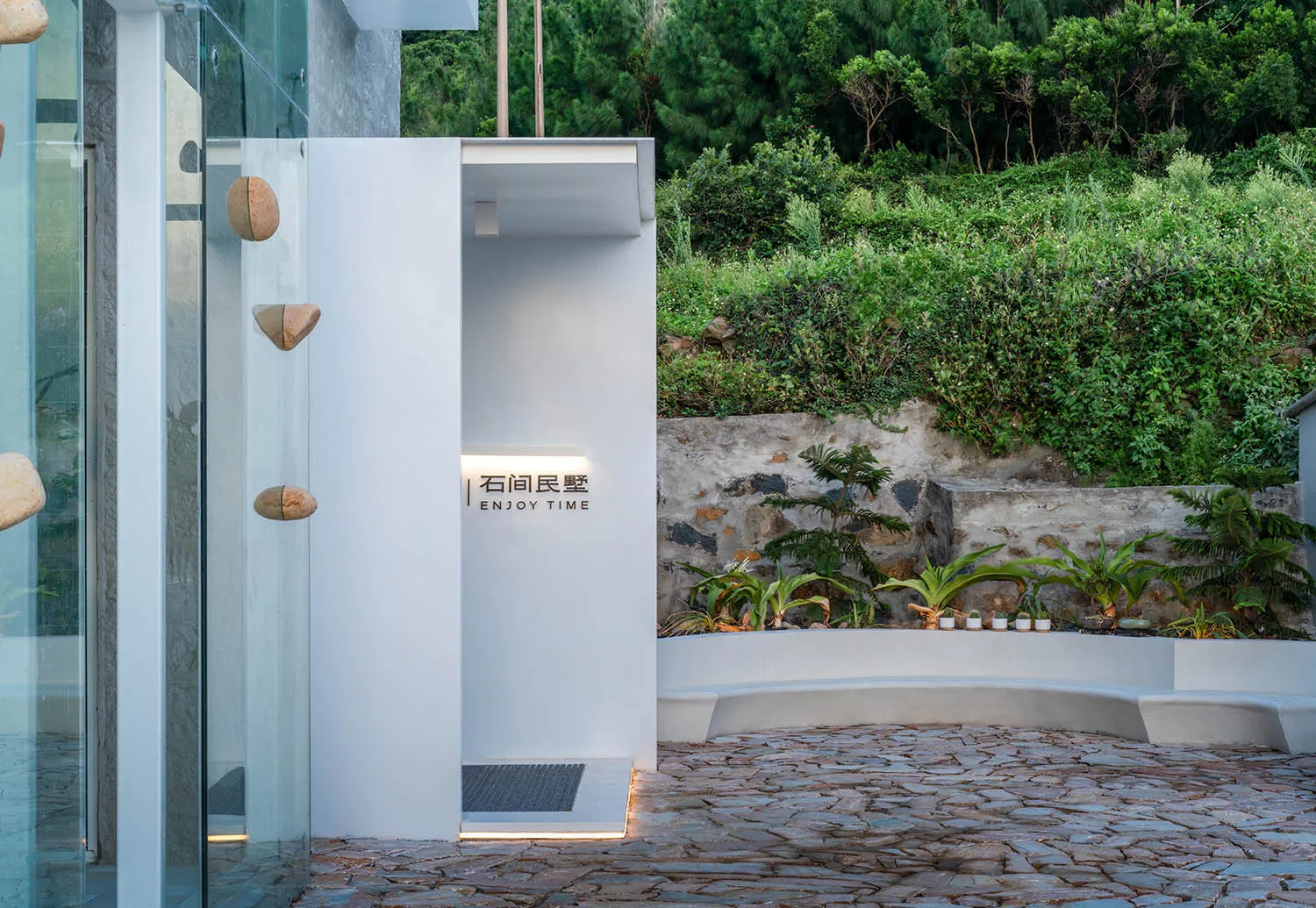 A minimalist entranceway with concrete walls and a stone pathway leading to a green landscape.