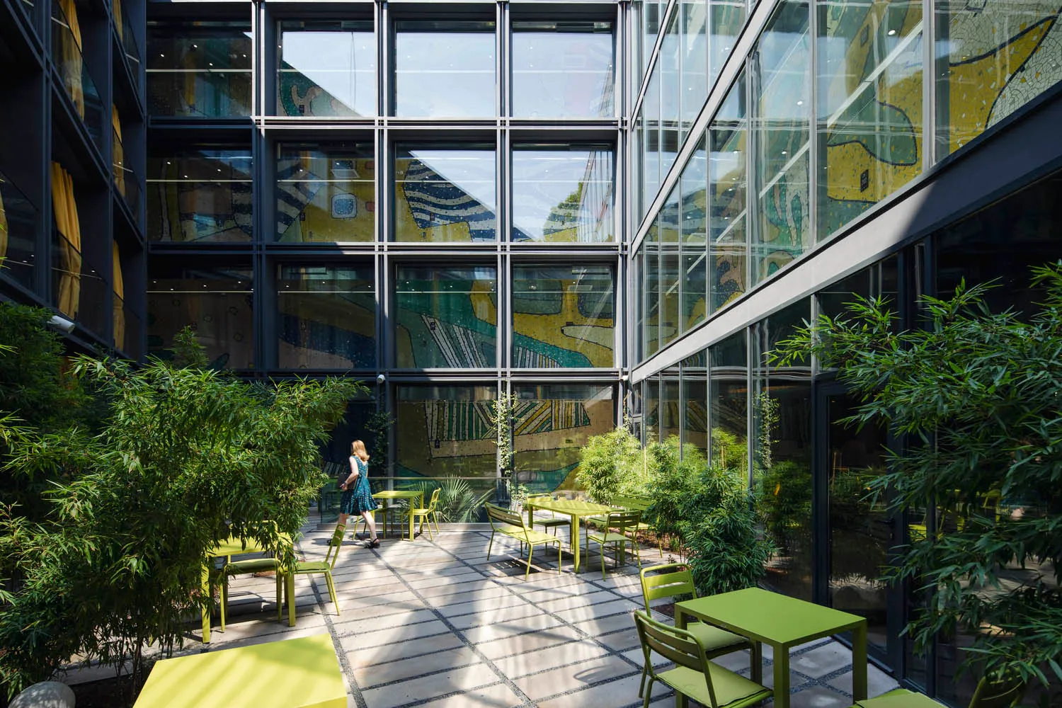 An indoor green space with modern furniture, glass walls, and potted plants.