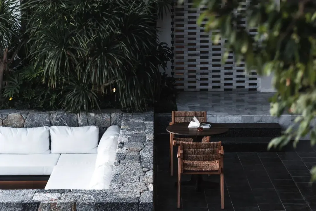A modern interior space featuring a white sectional sofa, a wooden table with a book and small plant, and a wall made of natu