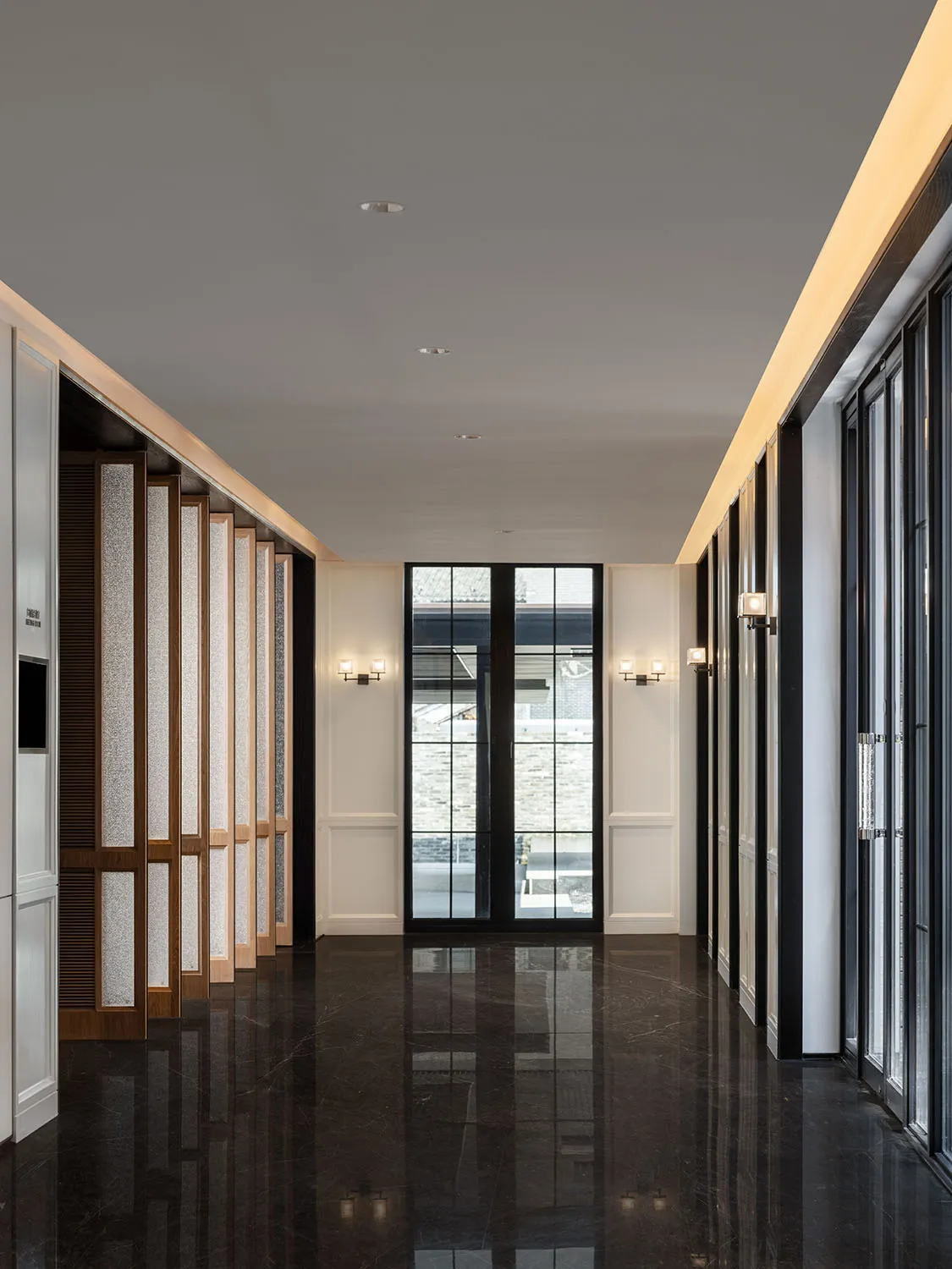 A minimalist corridor featuring dark marble flooring and walls, with sconces and large windows.