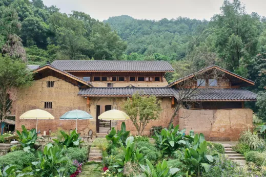 A clay-clad house with a terracotta roof and wooden accents on a hilly landscape.