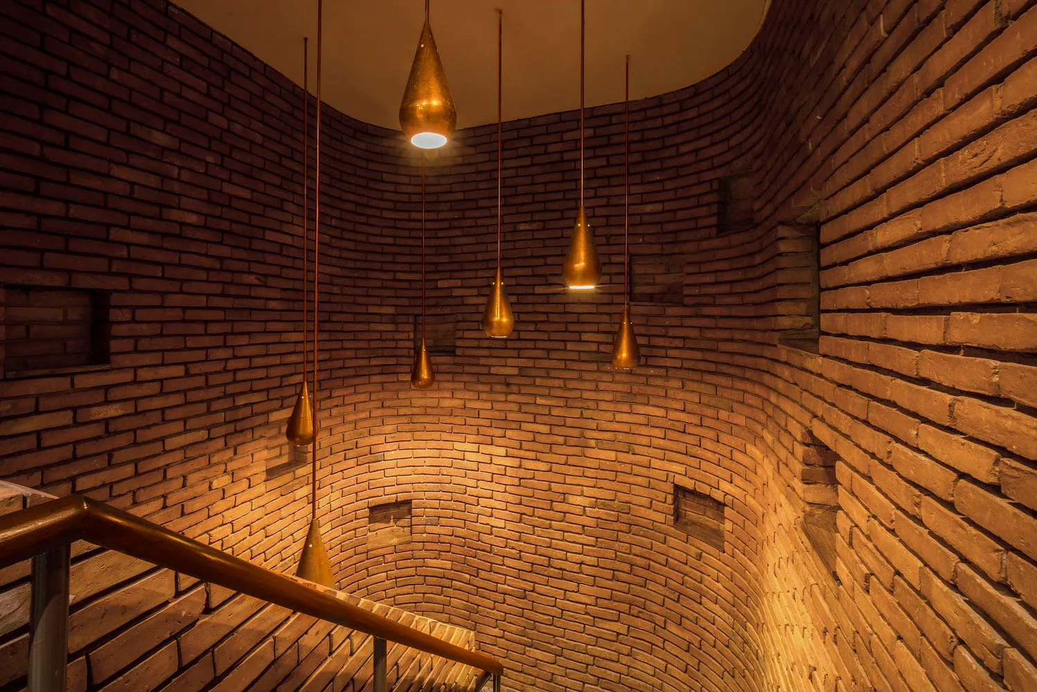A modern industrial staircase with brick walls and hanging lights.