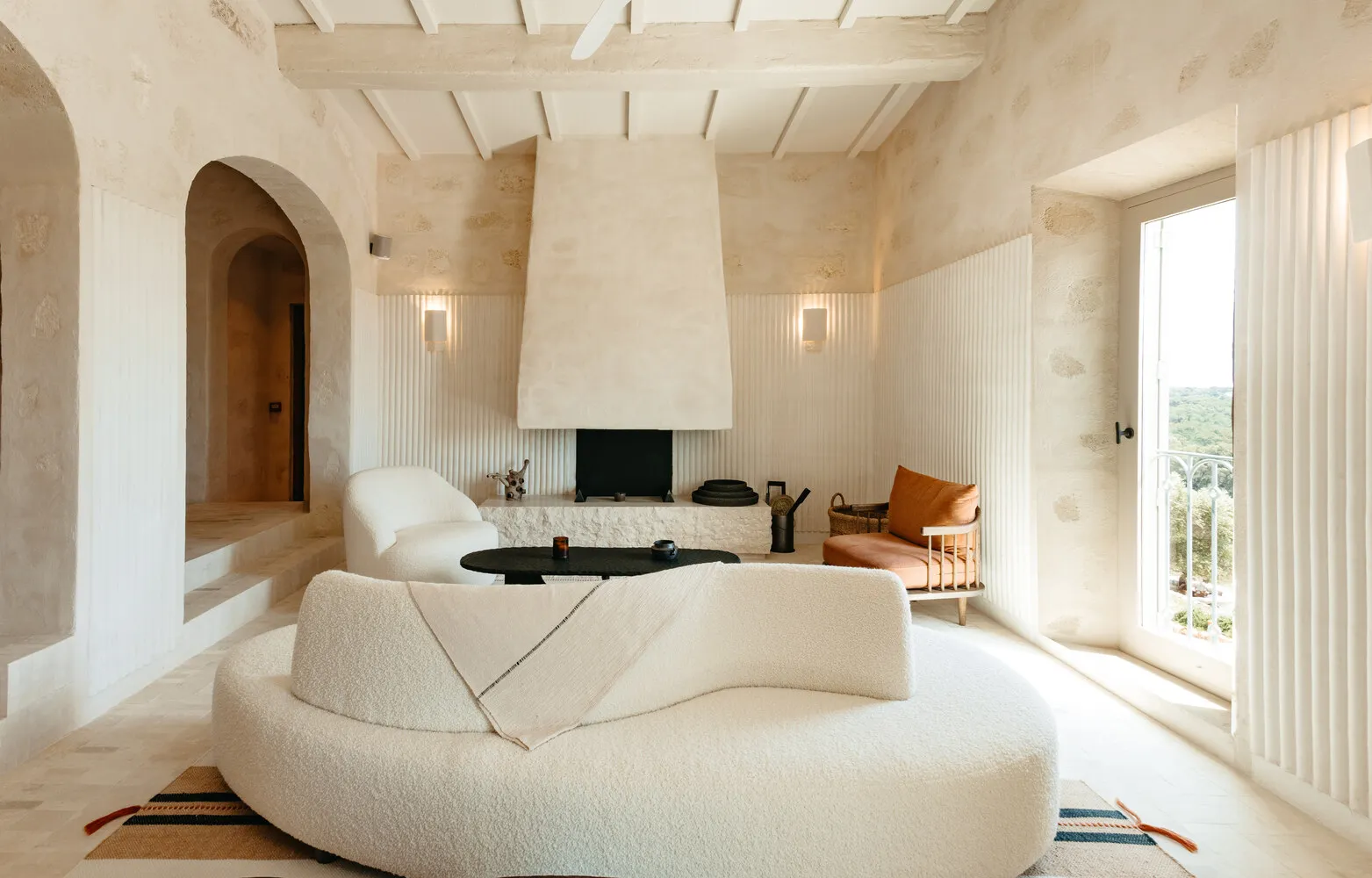 A minimalist living room with a round white sofa, a white armchair, and a concrete fireplace.