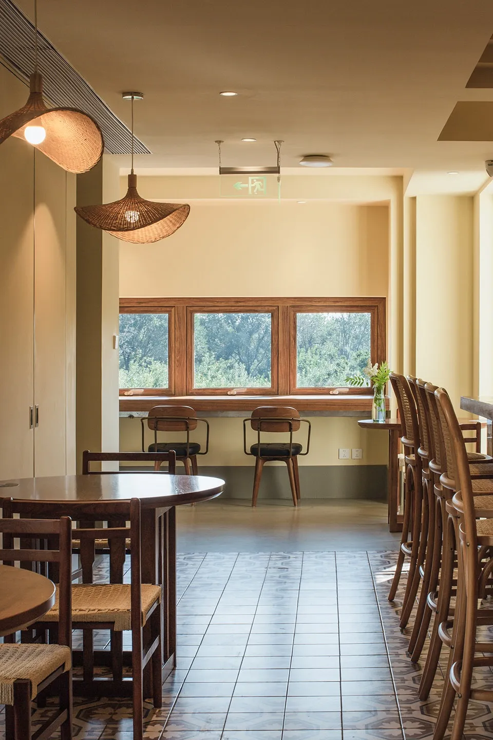 A minimalist restaurant interior with wooden furniture and large windows overlooking a green landscape.