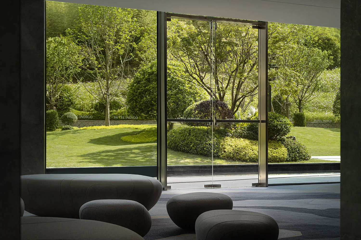 A modern hotel lobby featuring glass, concrete, and greenery