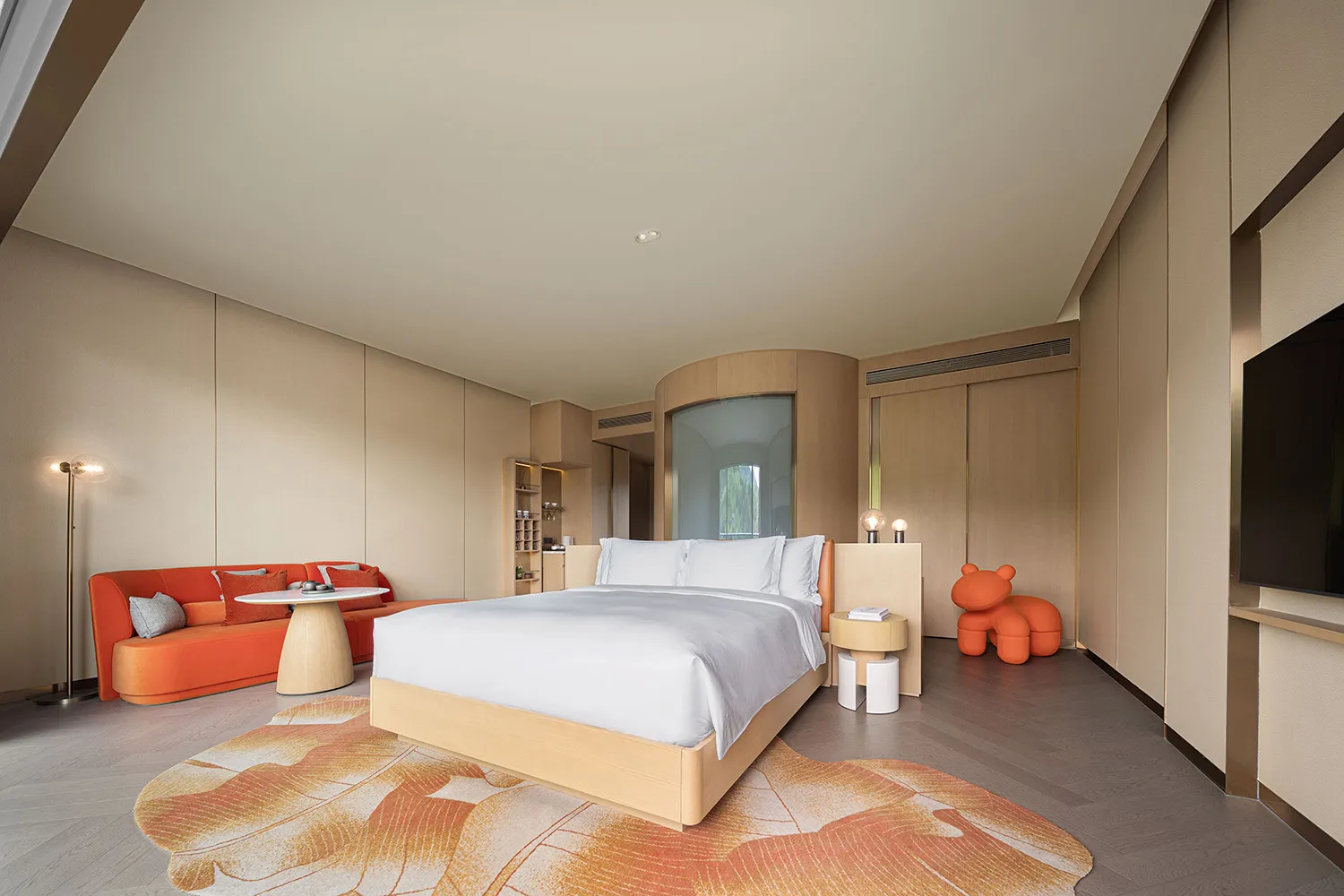 A modern minimalist bedroom featuring a bed with a wooden frame, white bedding, and an orange couch with pillows under a beig