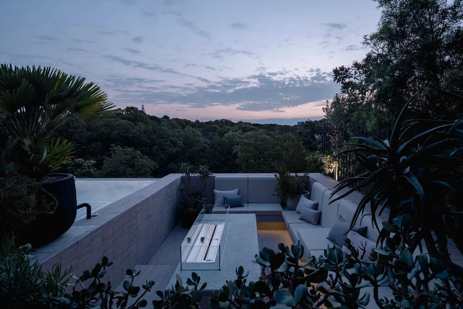 Modern outdoor lounge area with concrete, metal, and glass elements. Includes seating, cushions, and a fire pit.