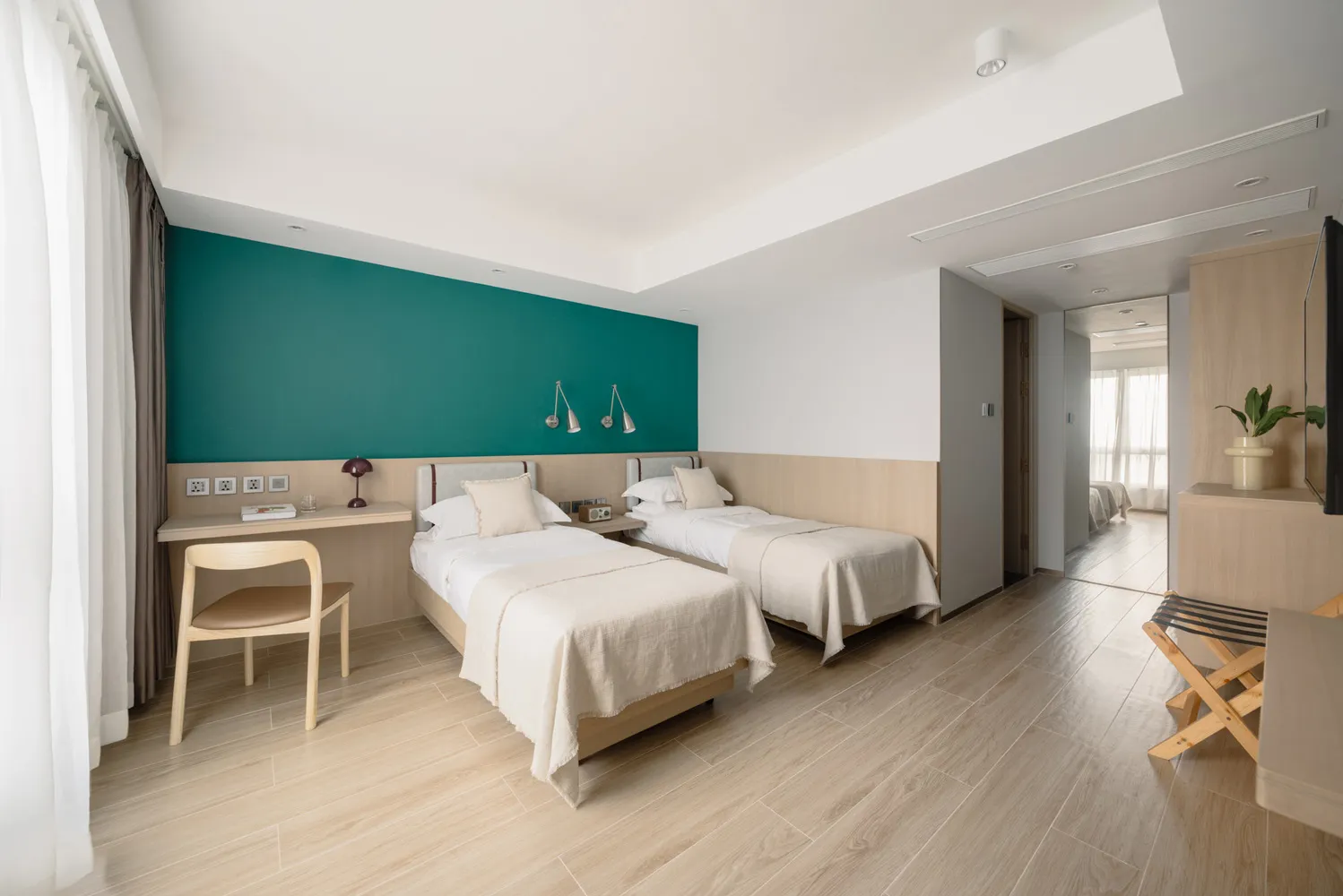 A modern minimalist bedroom with twin beds, wooden headboards, and a green accent wall.