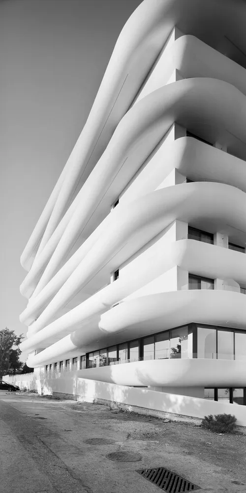 Modern white building with curved balconies and white walls in front of a clear sky.