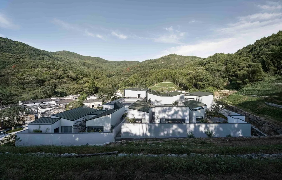 White residential villas with green roofs nestled among green hills.