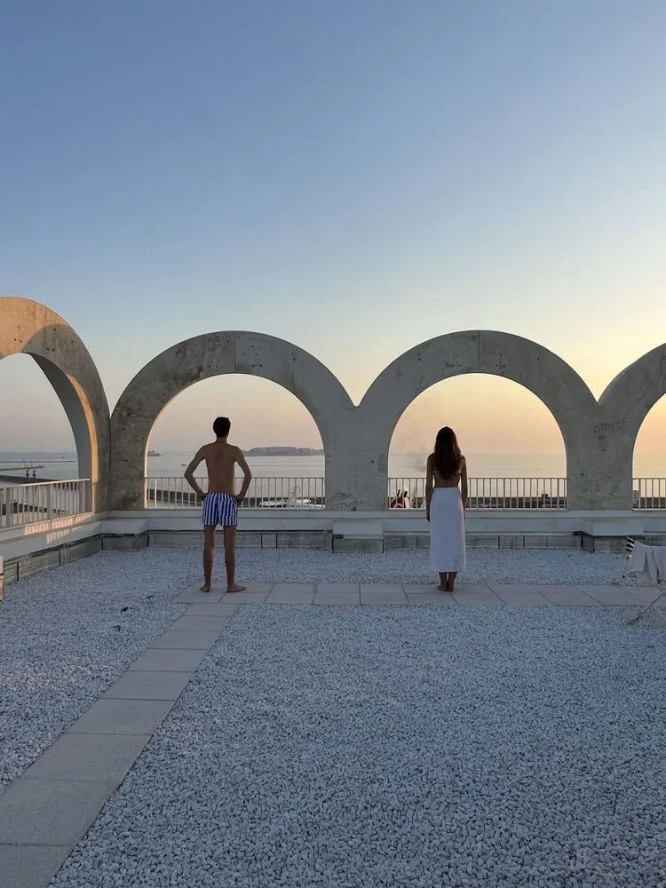 People standing in front of arches overlooking the sea at sunset.