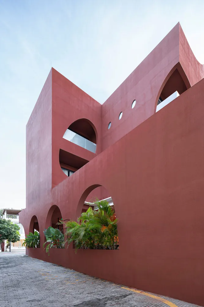 Modern building with a red concrete facade featuring arched windows and balcony.