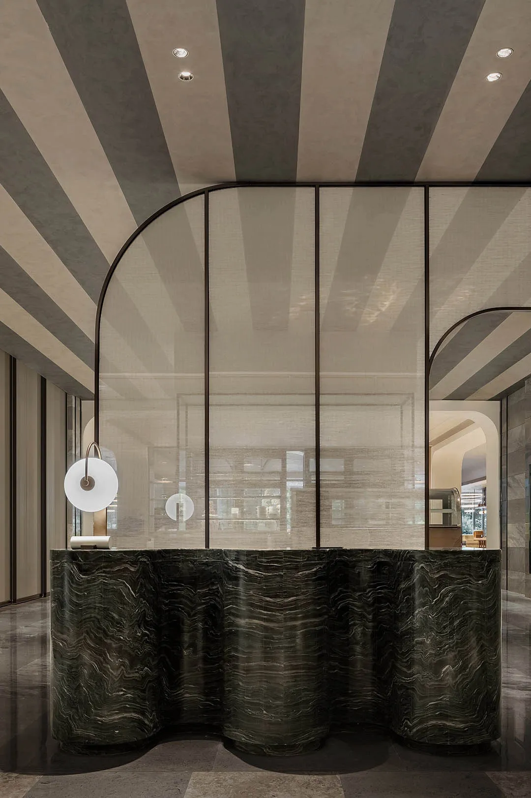 Modern lobby with glass partition and curved edges, featuring sleek design and sophisticated materials.
