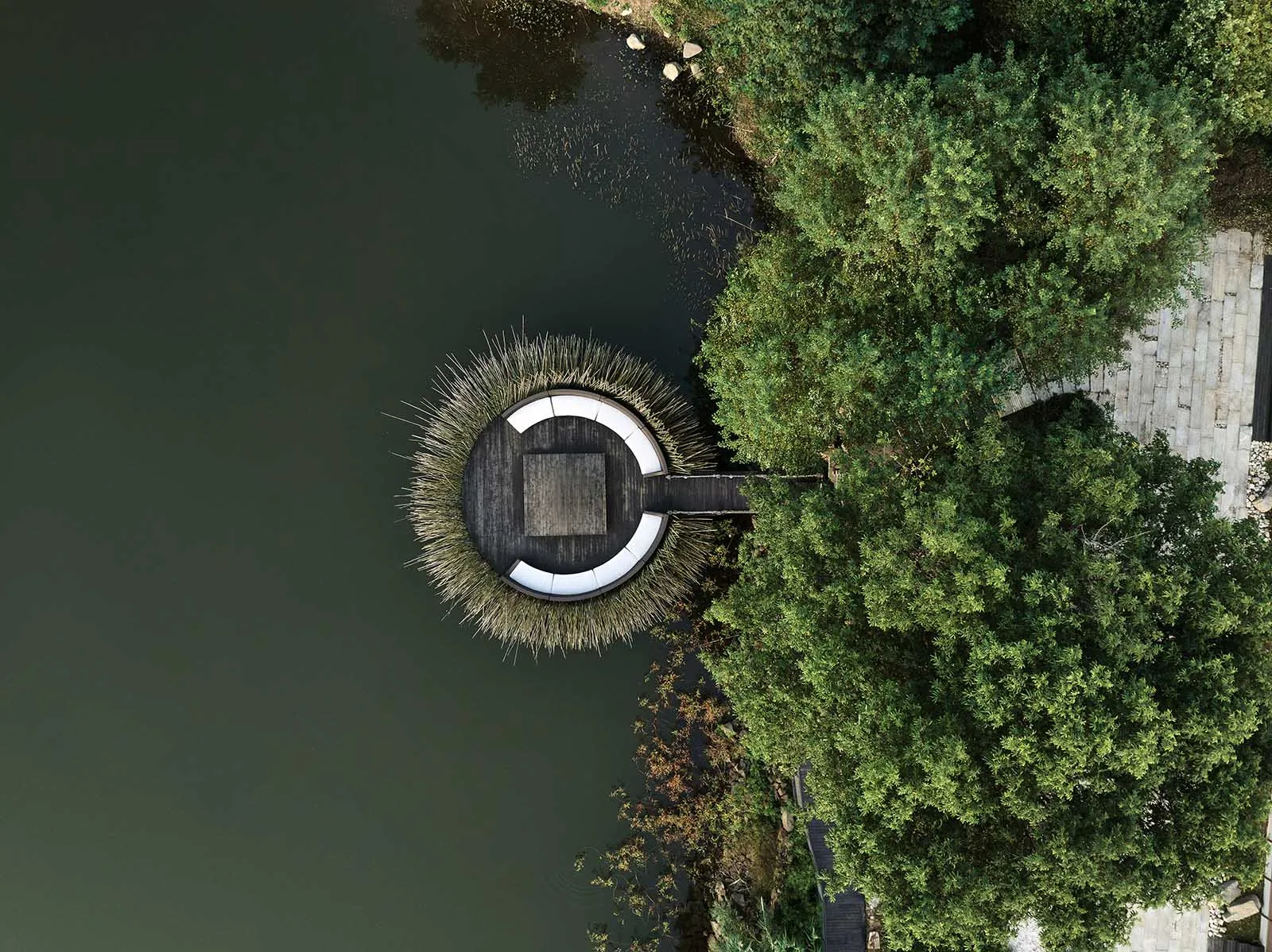 A circular floating platform made of reeds on a serene lake surrounded by lush greenery.
