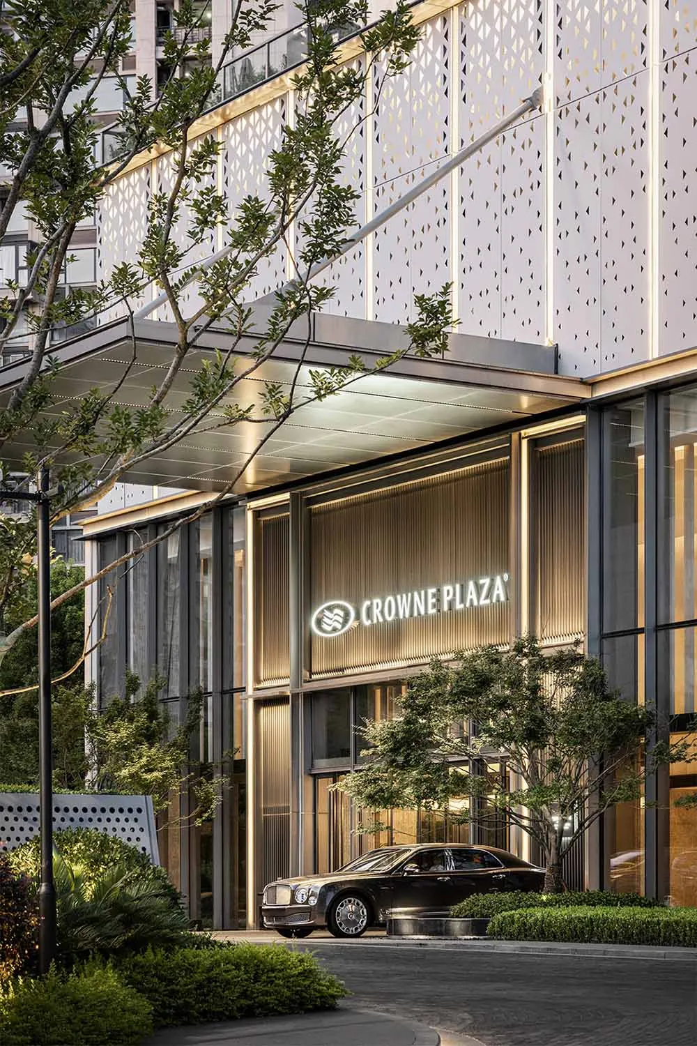 Modern hotel exterior featuring metal and glass materials, surrounded by green landscaping.