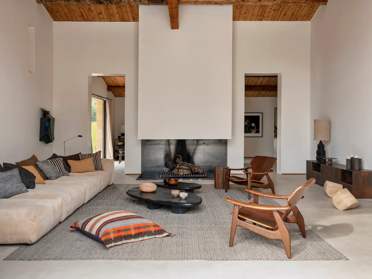 A modern minimalist living room with a wooden beam ceiling, a long sofa, and a fireplace.