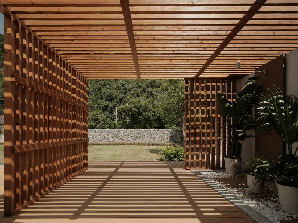 A modern wooden patio garden space featuring lattice walls, greenery, and a stone wall in the background.