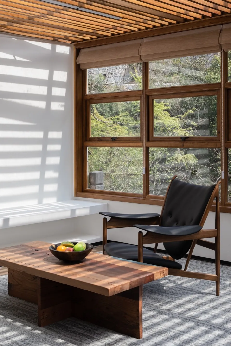 Modern living room with white walls, a wooden table, a black leather chair, and a bowl of fruit.