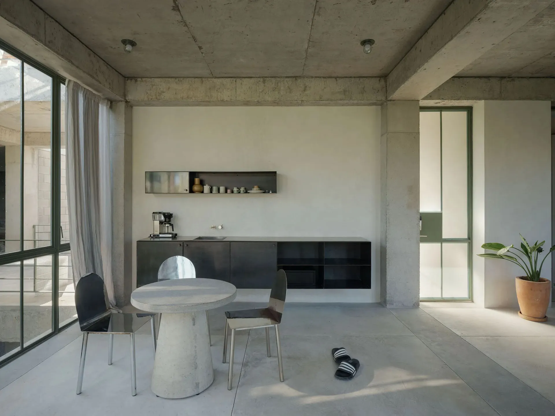 A minimalist residential kitchen featuring concrete finishes and a concrete dining table.
