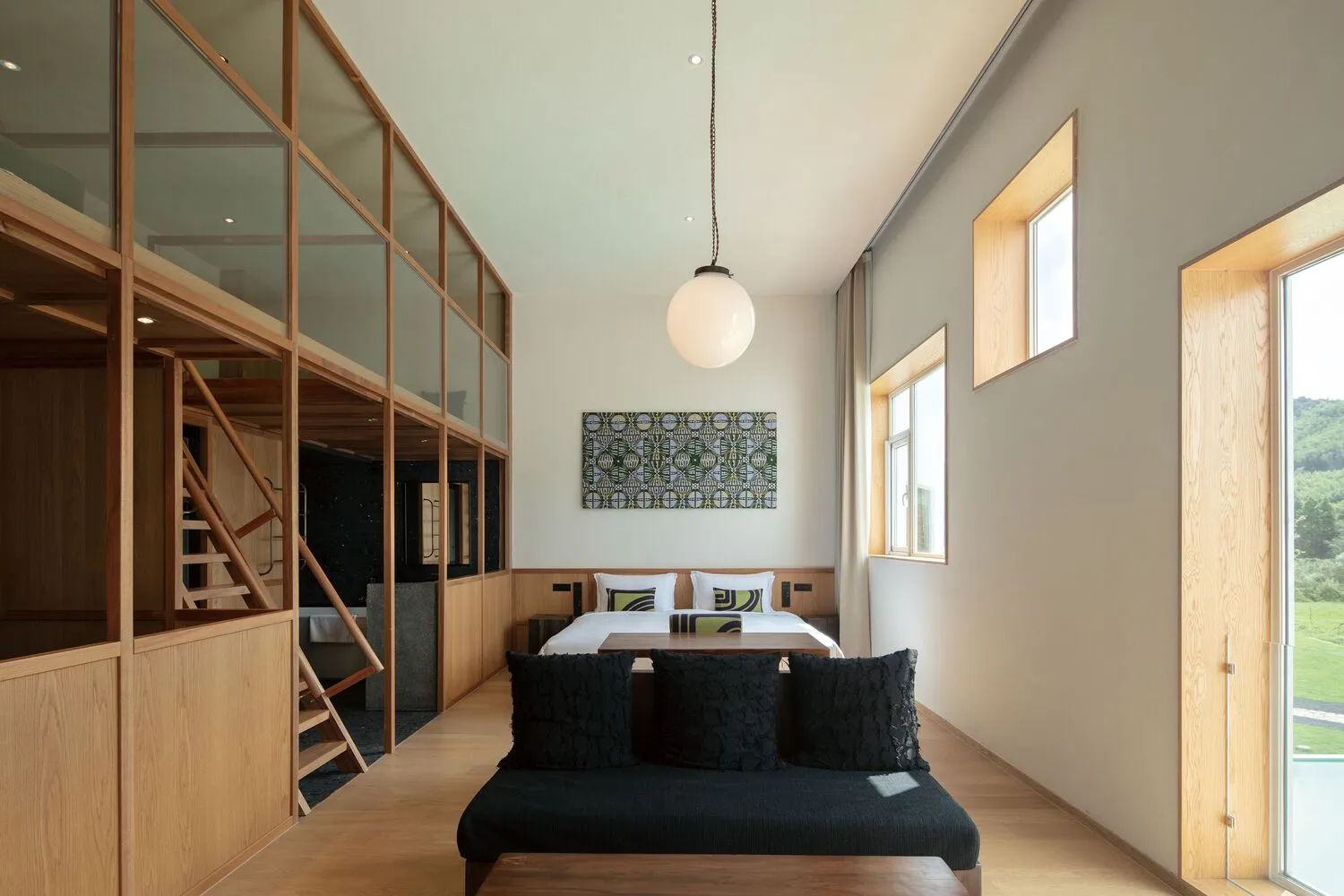 A modern bedroom featuring a bed with a minimalist design, black cushions, and a large window with natural light.