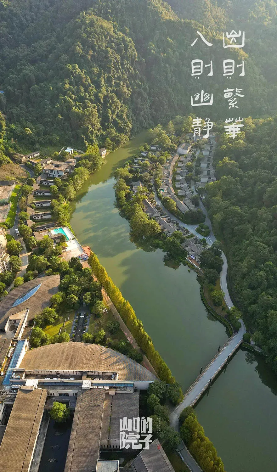 Aerial view of residential houses and buildings surrounded by lush greenery and a meandering river.